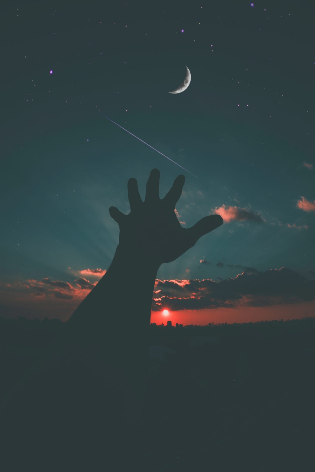 A hand is reaching up to the sky at sunset.
