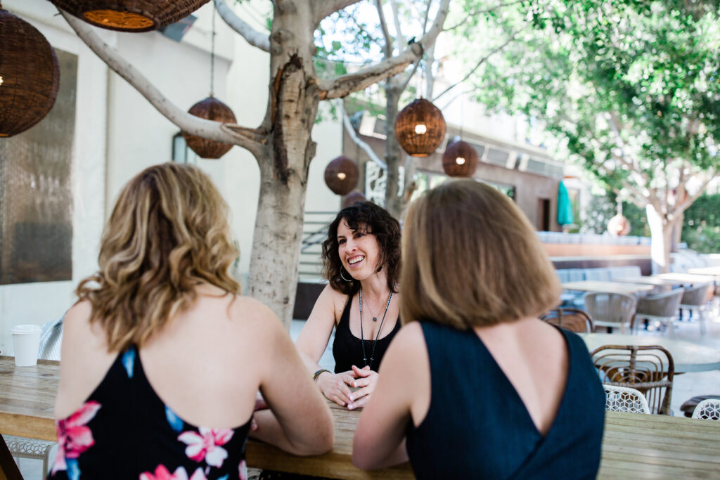 Three women sitting at a table talking to each other.